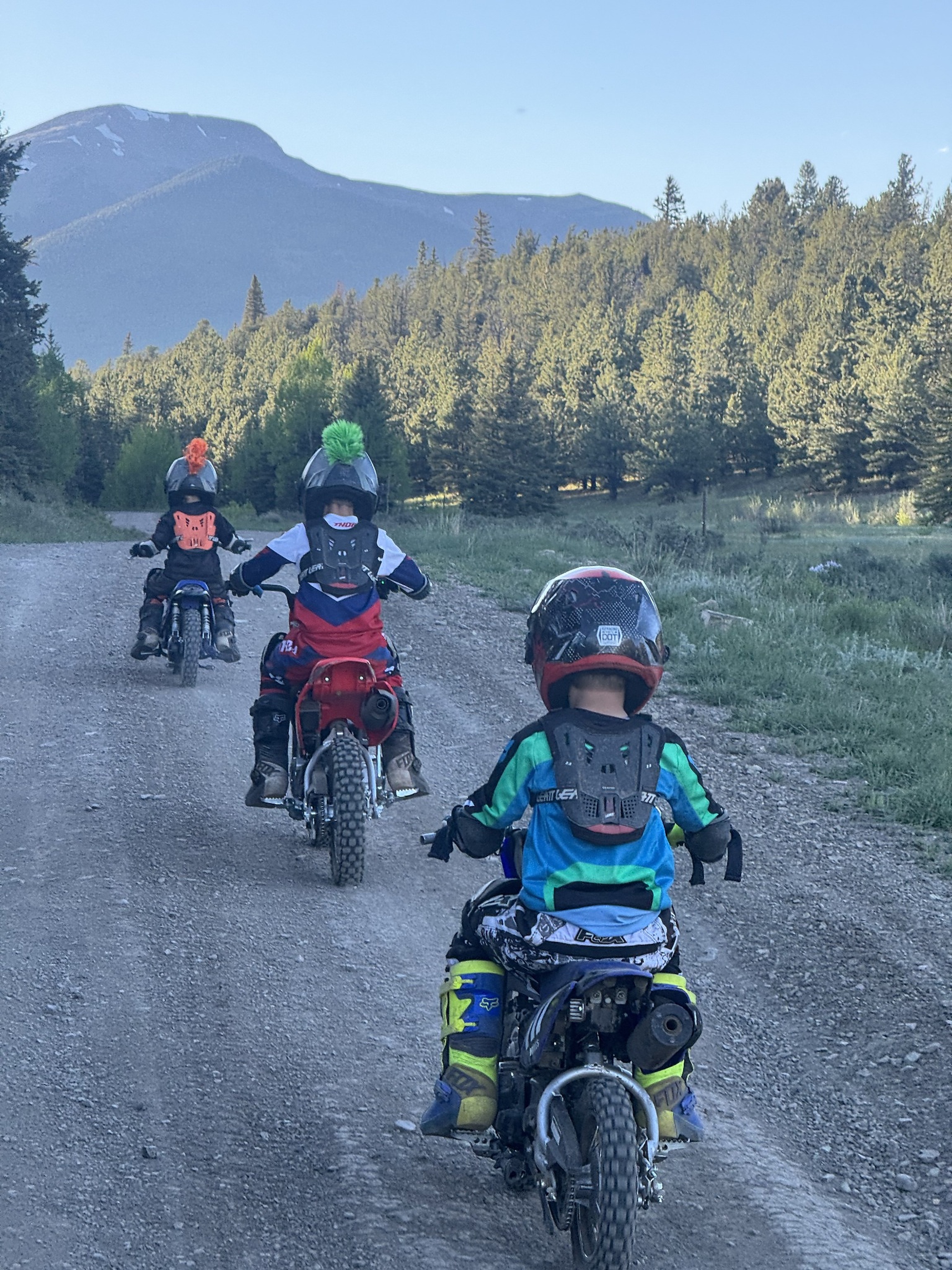 Three young riders on dirt bikes along a mountain road