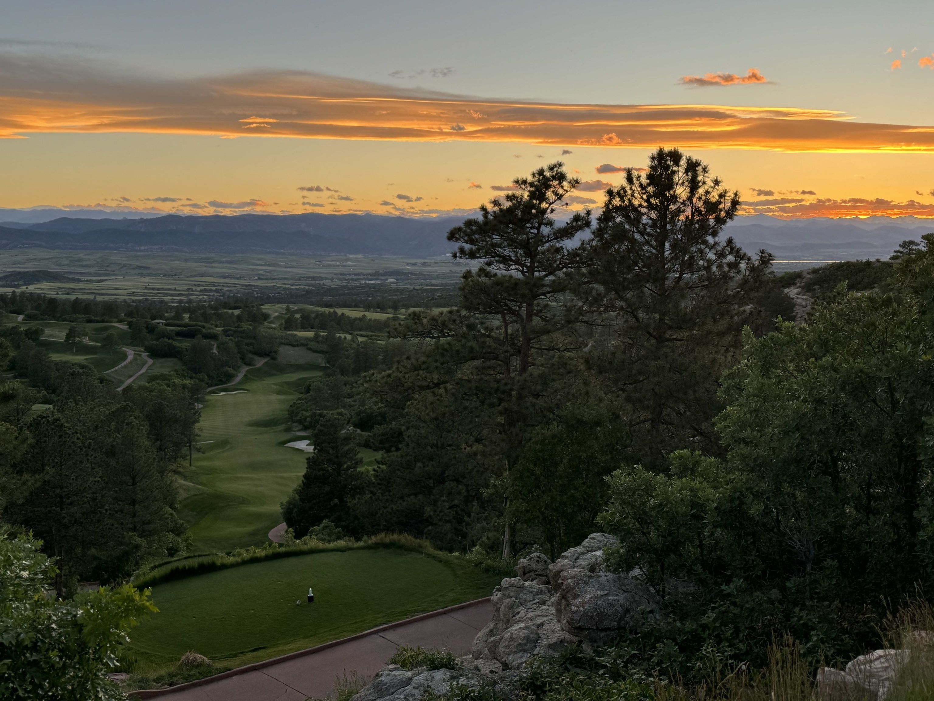 A golf course in the foothills beneath a glowing sunset